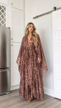 Front full-length view of woman wearing brown abstract animal print kimono maxi dress with western belt