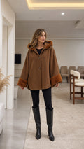 Front view of model wearing camel hooded cape coat with faux fur cuffs and black tall boots