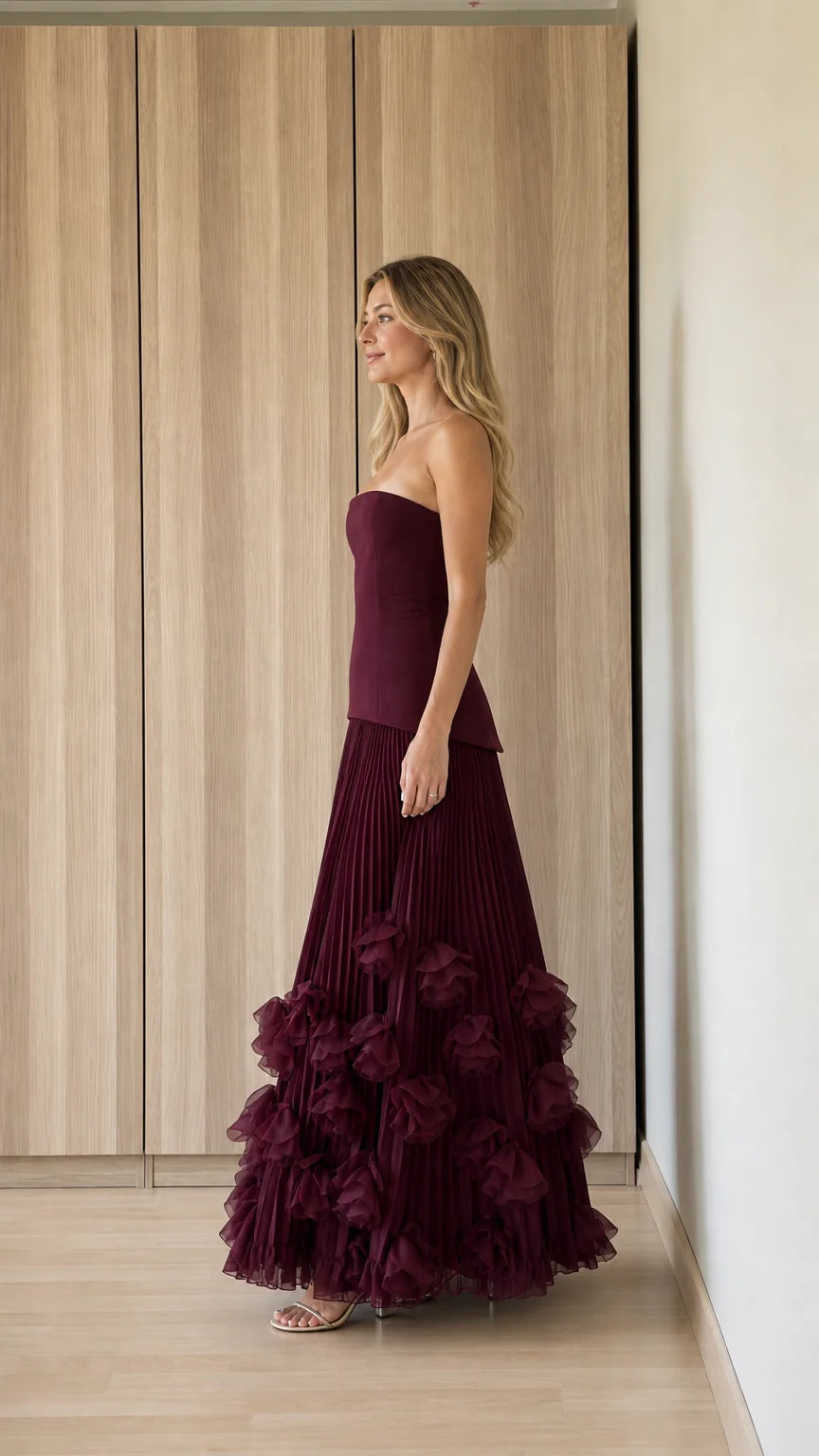 Side profile view of burgundy strapless pleated evening dress
