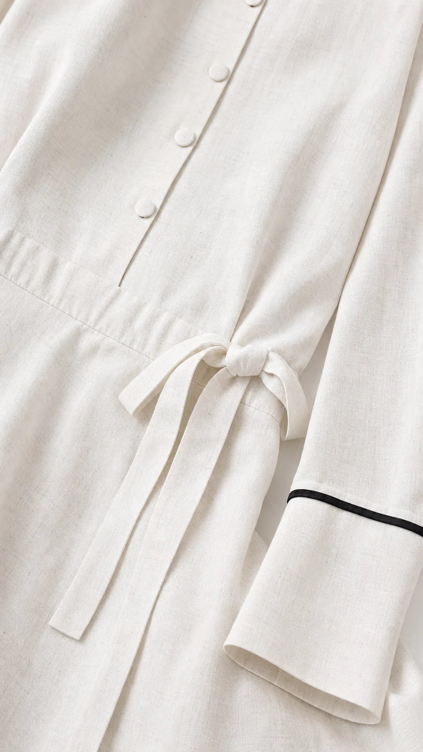 Close-up detail of button placket, cuffs, and waist tie on white dress