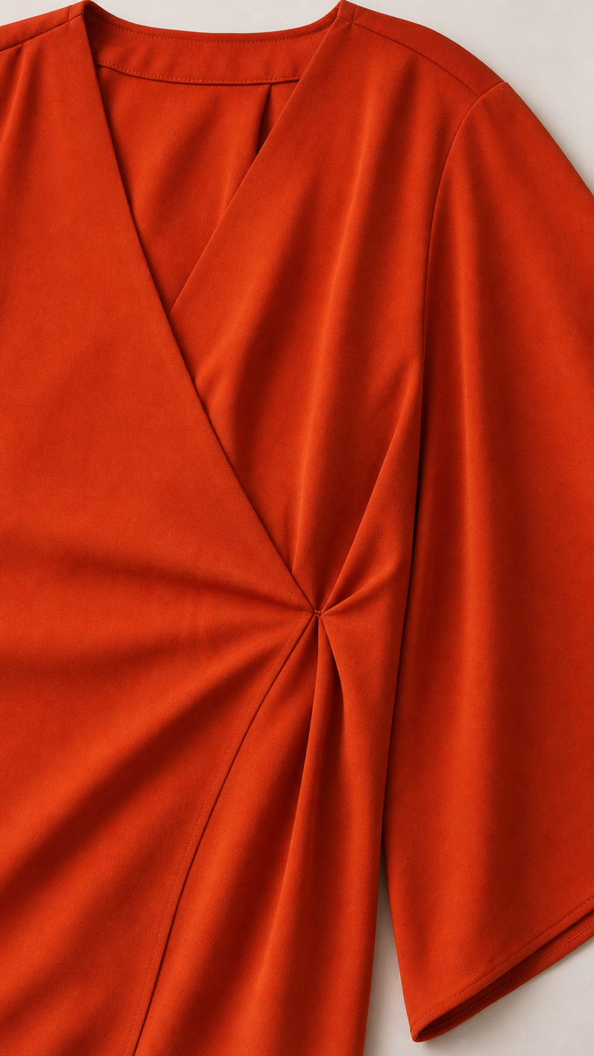 Close-up detail of side pleat and V-neckline on burnt orange wrap blouse