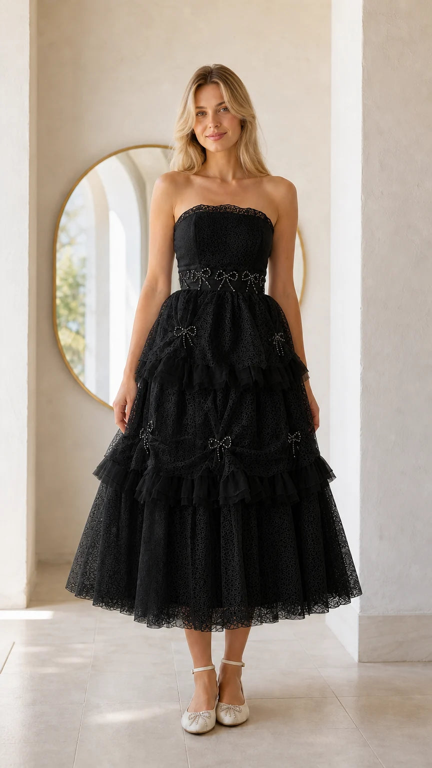 Front full view of woman wearing black strapless tiered midi dress